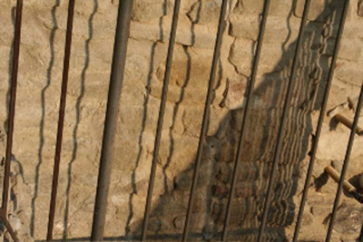 Straight railings casting rippled shadows on a rough stone wall.